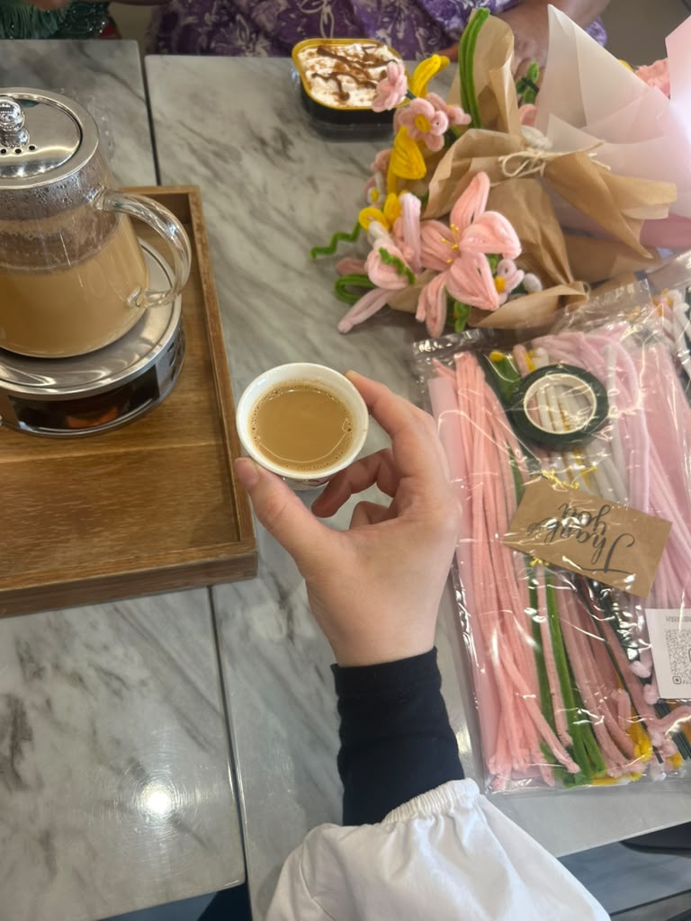 A hand holding a small cup of tea beside handmade flower bouquets and craft kits